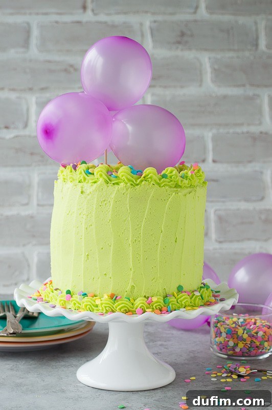 Homemade funfetti cake with lime green buttercream! Top the cake with a DIY balloon cake topper! A close-up shot of the vibrant green frosting, colorful sprinkles, and whimsical purple balloon topper, ready for a party.