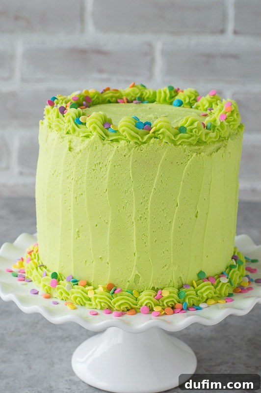 Homemade funfetti cake with lime green buttercream! A beautiful side view of the frosted cake, showcasing its smooth, zesty green texture and festive sprinkles around the base.