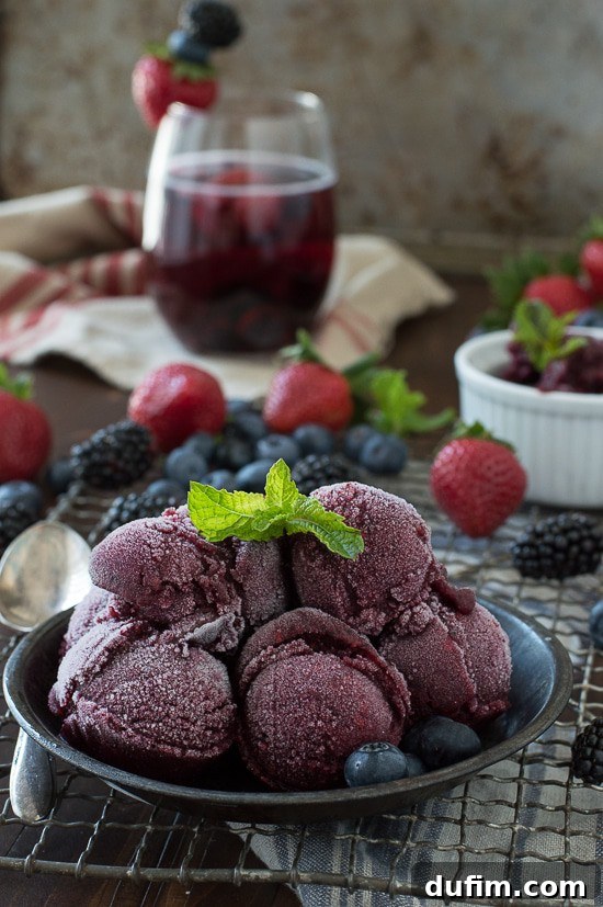 Homemade Berry Sangria Sorbet garnished with fresh mint, surrounded by a vibrant mix of strawberries, blueberries, and blackberries.