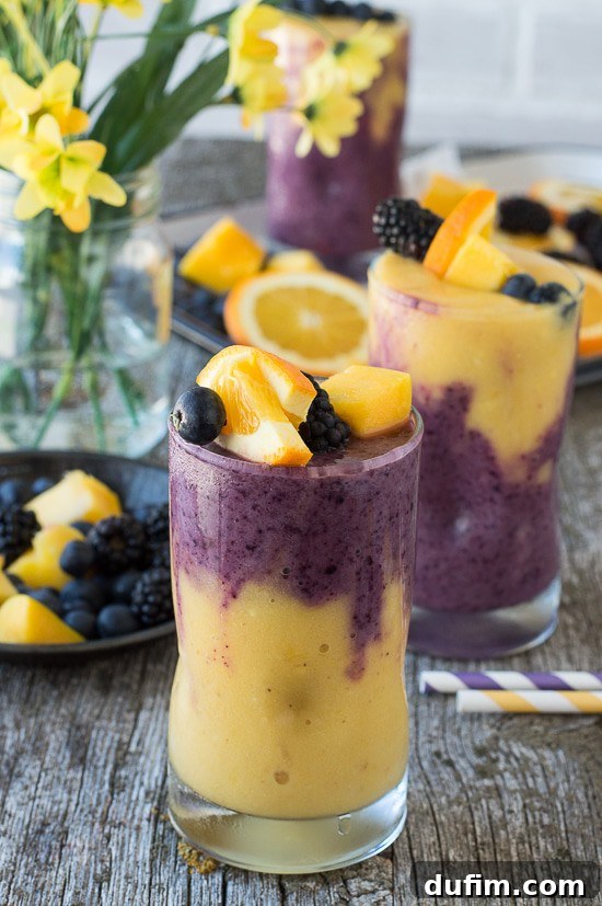 A stunning two-layer Hawaiian Berry Smoothie featuring a bright orange mango layer and a deep purple berry layer, garnished with fresh fruit skewers, presented in an elegant glass.