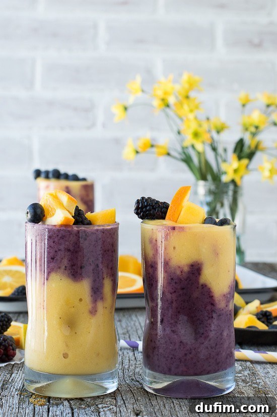A tall glass of two-layer Hawaiian Berry Smoothie, showing distinct orange mango and berry layers, beautifully garnished with a skewer of fresh fruit.