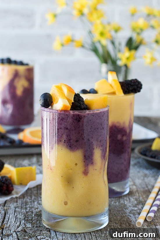 A visually appealing two-layer Hawaiian Berry Smoothie in a glass, with vibrant orange and purple colors swirling together, garnished with fresh berries and an orange slice.