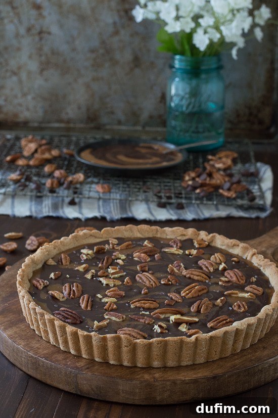 A close-up view of the irresistible Turtle Tart, showing the intricate swirls of golden caramel and dark chocolate, speckled with whole and broken pecans.