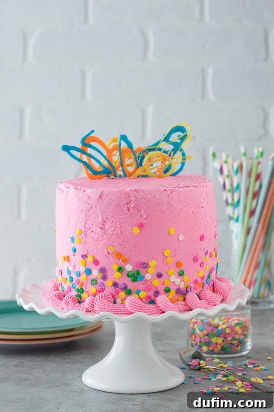 A beautifully decorated Pink Confetti Chocolate Chip Cake with smooth pink buttercream, colorful confetti sprinkles, and elegant chocolate swirl decorations on top. The cake is moist and promises a delightful flavor.
