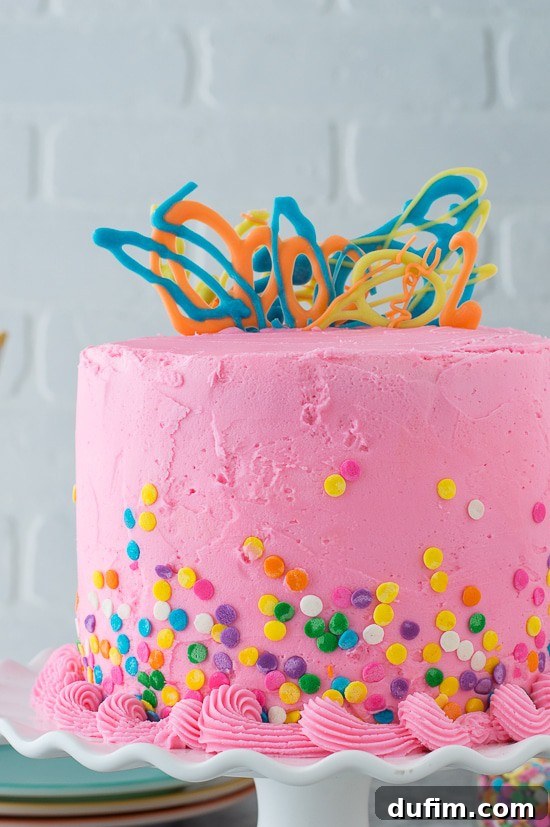 A close-up shot of a slice of Pink Confetti Chocolate Chip Cake, showcasing the tender white cake flecked with mini chocolate chips, layered with smooth pink buttercream.