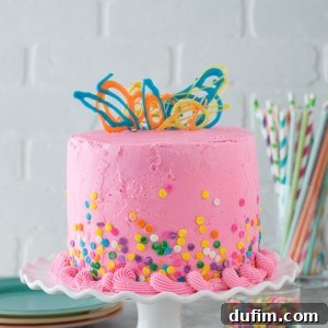 A stunning Pink Confetti Chocolate Chip Cake with pink buttercream and colorful sprinkles, ready for any celebration. Inside, it's packed with mini chocolate chips.