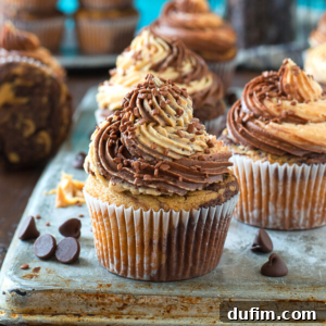 A close-up of chocolate peanut butter cupcakes with swirled chocolate and peanut butter frosting, topped with chocolate sprinkles, sitting on a metal tray with scattered chocolate chips.