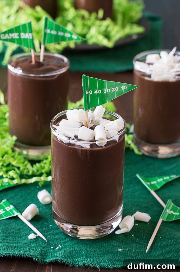 Two football pudding cups on a rustic wooden board, decorated with white laces, chocolate curls, and tiny 'Game Day' flags.