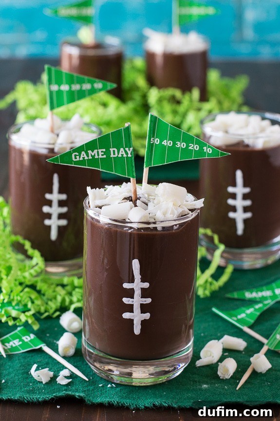 A styled photo featuring a hand holding a football pudding cup, highlighting the vibrant green background and festive theme.