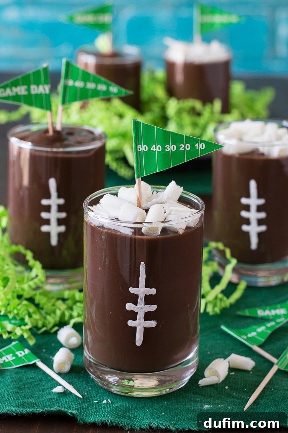 Six football pudding cups arranged in a festive setting, showcasing various angles and garnishes, including mini football picks and chocolate curls.