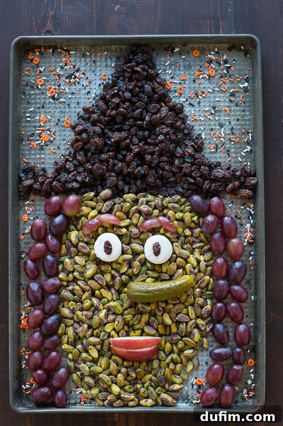 Full assembly of the Halloween Witch Platter, featuring the complete witch's face with raisin hat, pistachio skin, marshmallow eyes with raisin pupils, pickle nose, apple slice mouth, and red grape hair.