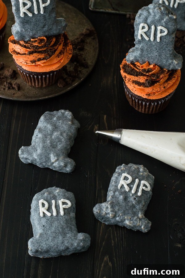 A close-up view of a Halloween Tombstone Cupcake, showcasing the intricately designed Rice Krispie treat tombstone and the fluffy orange buttercream frosting.