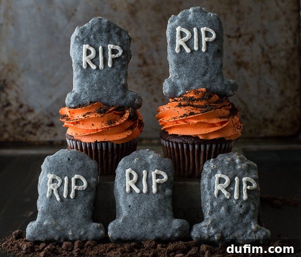 Two irresistible Halloween Tombstone Cupcakes, displaying the speckled chocolate coating on the Rice Krispie tombstones and the expertly piped buttercream.
