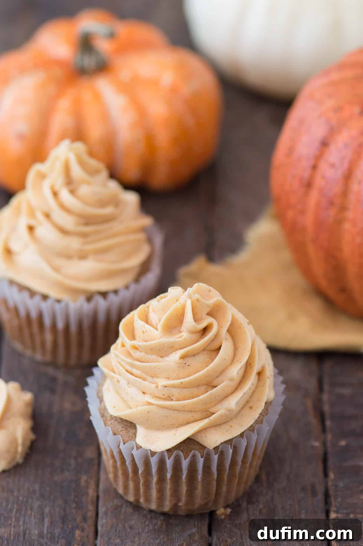 pumpkin cupcake with pumpkin frosting on wooden background with pumpkins in background