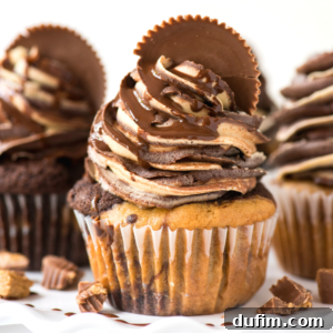 Reeses cupcakes topped with swirled chocolate frosting, chocolate drizzle, and a peanut butter cup piece, with small peanut butter cups scattered around.