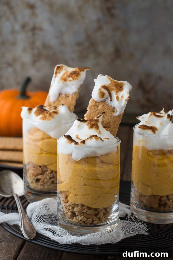 Spiced Pumpkin Cheesecake Parfaits 5 Four pumpkin pie cheesecake shooters lined up, featuring a rustic presentation with pumpkins and crackers in the background.