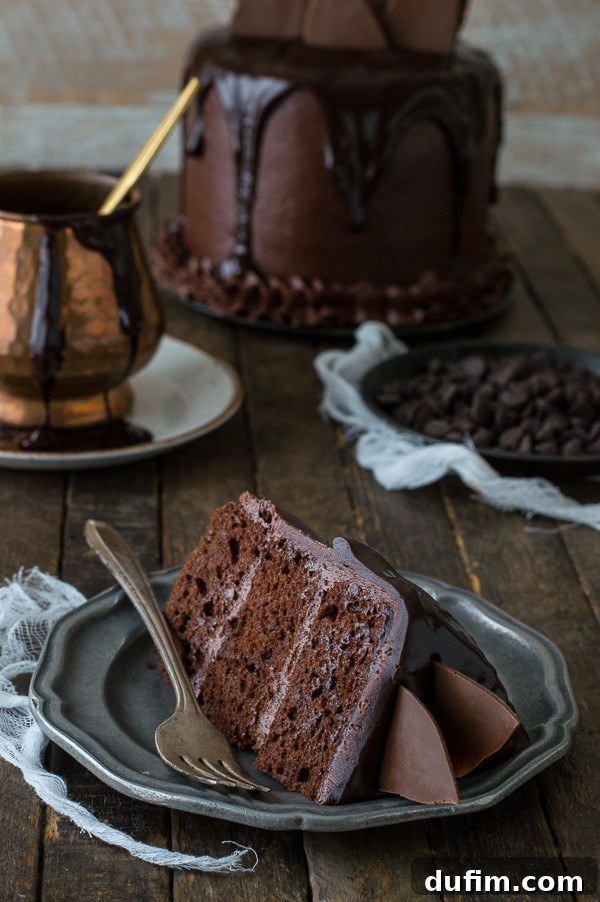 A slice of Chocolate Chocolate Cake with chocolate ganache and chocolate shatters on a small serving plate.