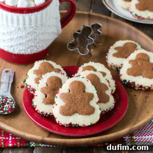 A red plate holds festive gingerbread men slice and bake cookies with colorful sprinkles on the edges; a mug with a white knitted cover, cookie cutters, and a measuring spoon with sprinkles are nearby.