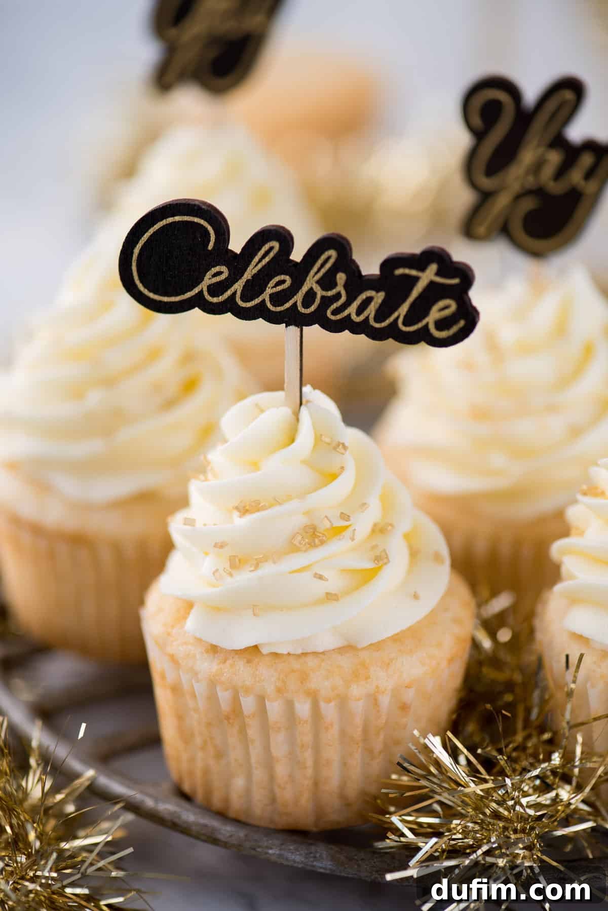 Easy champagne cupcakes with champagne buttercream, topped with dazzling gold sprinkles and a 'Celebrate' cupcake topper, ready for a New Year's Eve party.