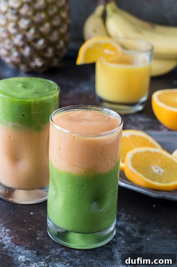 Close-up view of the layered green monster and orange smoothie, artfully topped with colorful fruit pieces on a skewer, against a rustic background.