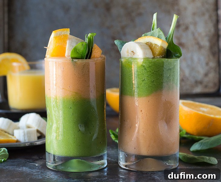 Overhead flat lay of a glass filled with the two-layer green monster orange smoothie, garnished with a colorful fruit skewer on a textured surface.