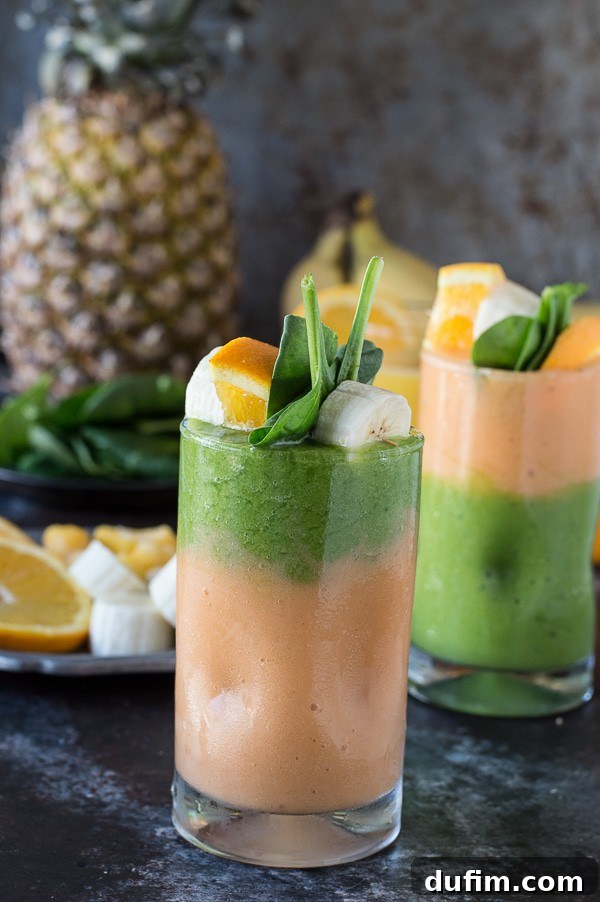 The two-layer green monster orange smoothie elegantly served in a glass, with a fruit skewer and a spoon, ready to be enjoyed as a wholesome treat.