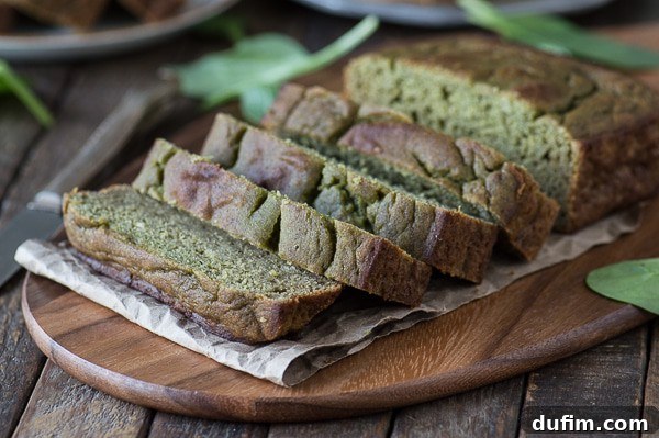 An overhead shot of a freshly baked loaf of green monster bread on a cooling rack, next to a stack of its delicious slices.