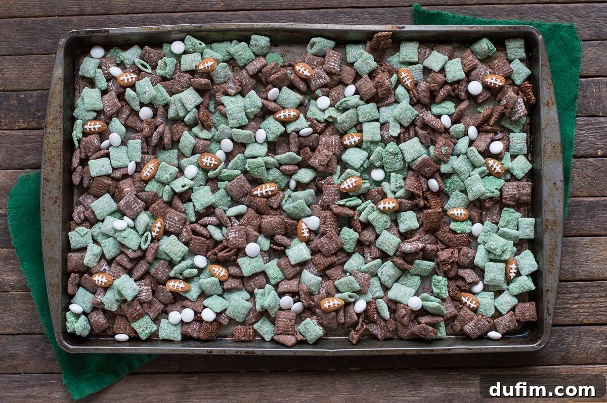 A baking sheet filled with mixed green and brown Football Puppy Chow, featuring almond footballs and small 'Game Day' flags.