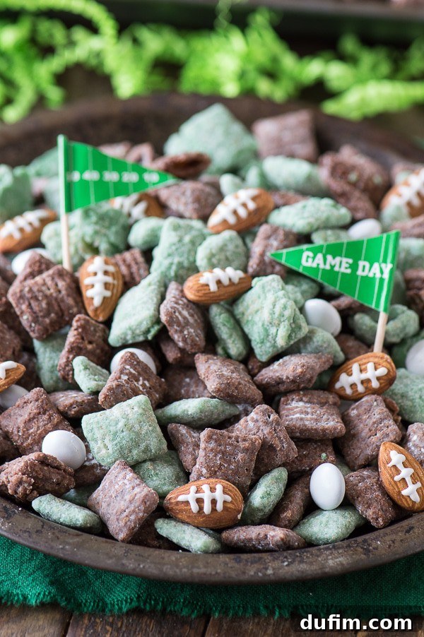 A large serving bowl filled with mixed green and brown Football Puppy Chow, adorned with almond footballs and 'Game Day' flags.