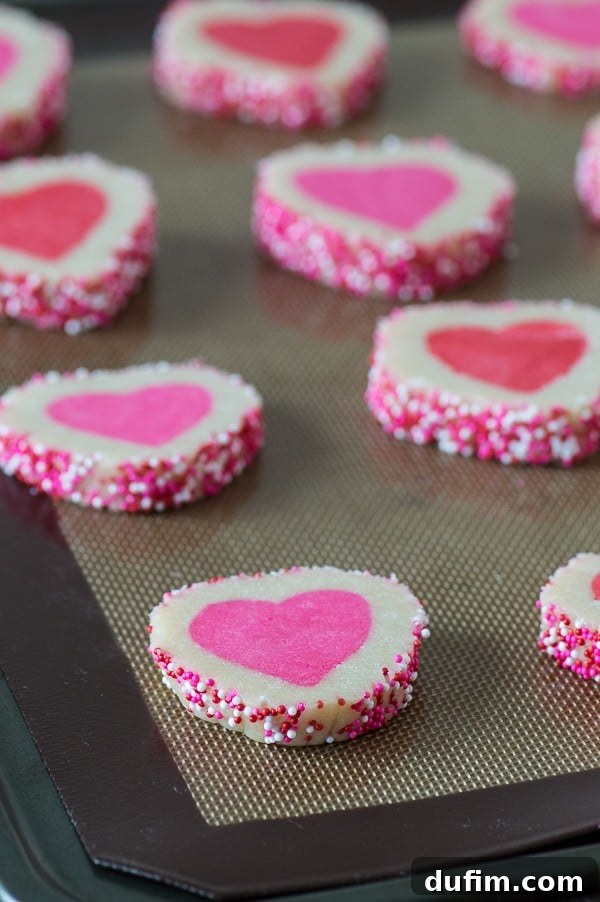 Ten Easy Homemade Valentine’s Day Slice N’ Bake Cookies covered in pink and white sprinkles on a baking sheet.