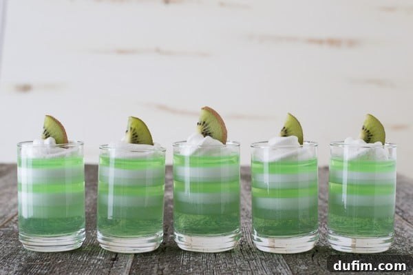 Five beautifully layered Melon Kiwi Jello Cups, garnished with fresh kiwi slices on a wooden table.
