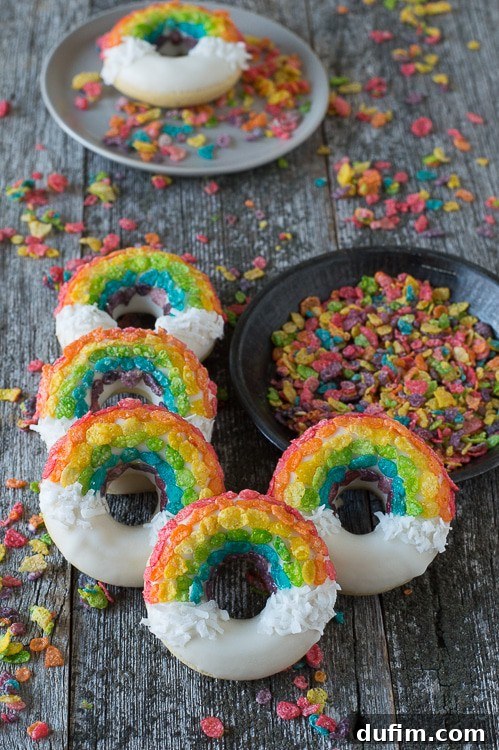 Five delightful Rainbow Donuts positioned next to a bowl of fruity pebbles on a charming wooden table.