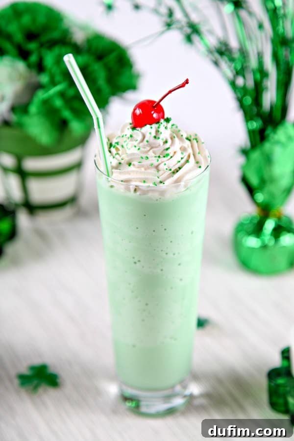 A frosty Homemade Shamrock Shake in a clear glass cup, crowned with a cherry and a charming white and green straw.