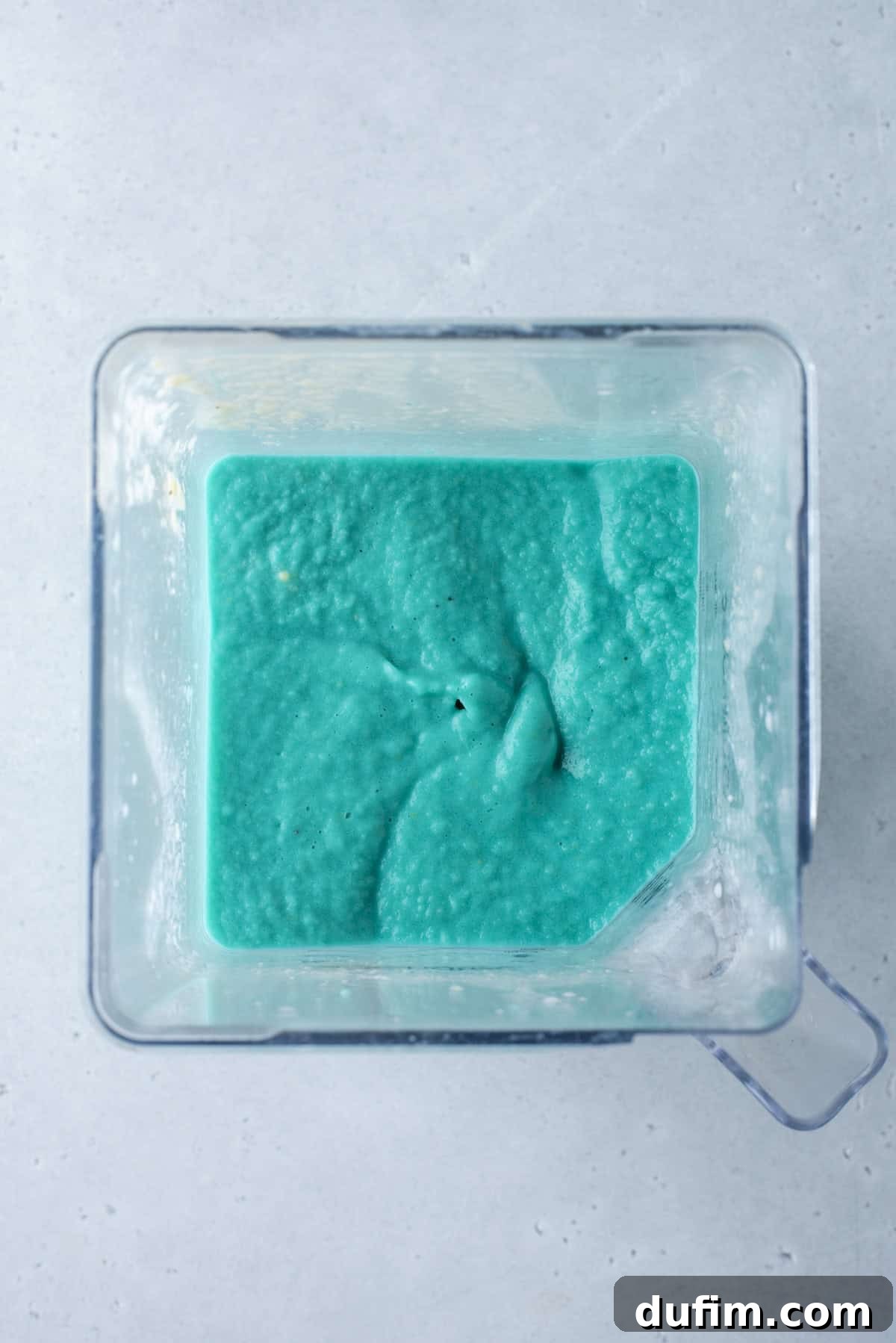A striking blue layer is gently spooned onto the green, creating a beautiful transition of color in the rainbow smoothie.