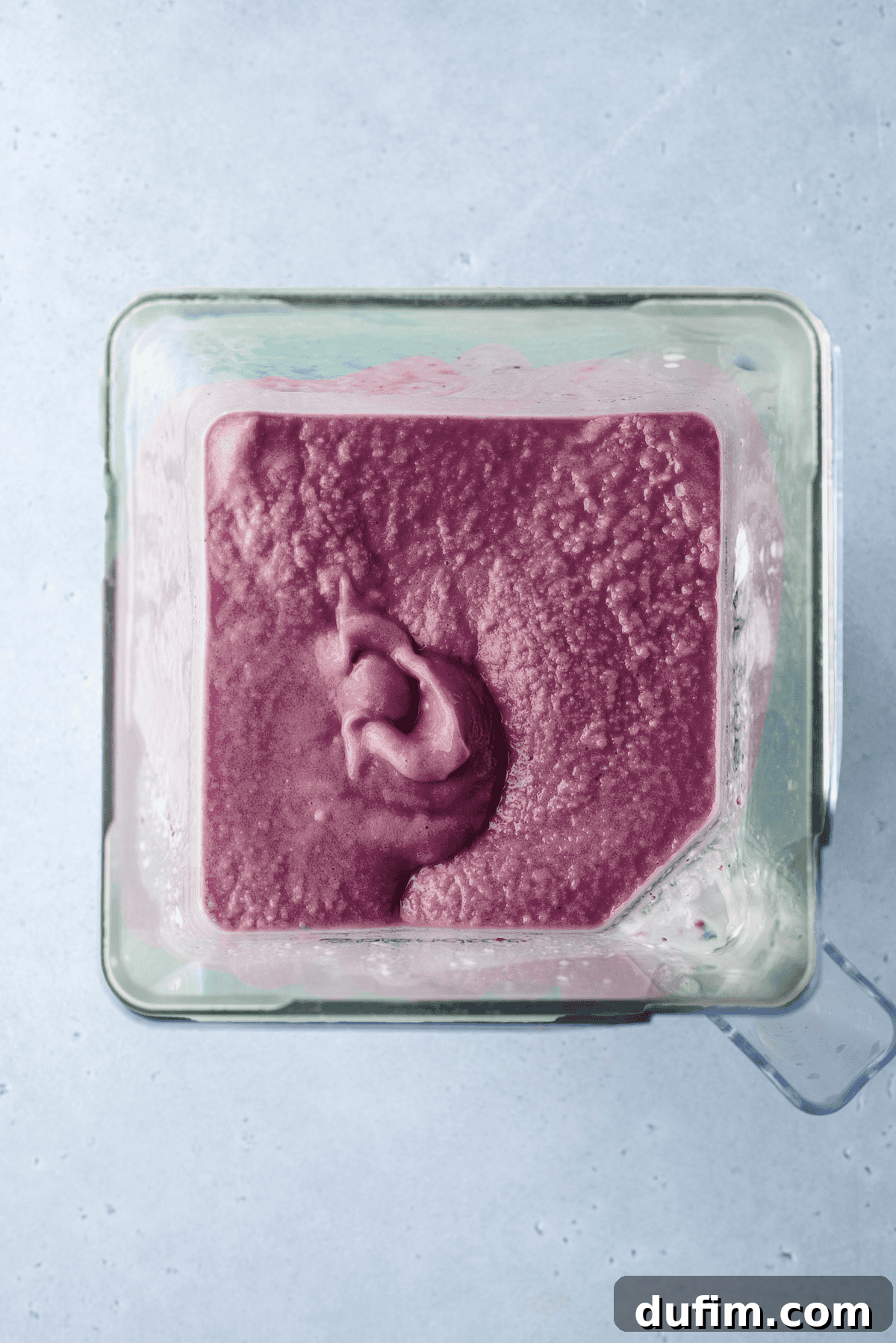 The final purple layer is carefully added to the top of the rainbow smoothie, completing the vibrant spectrum of colors.