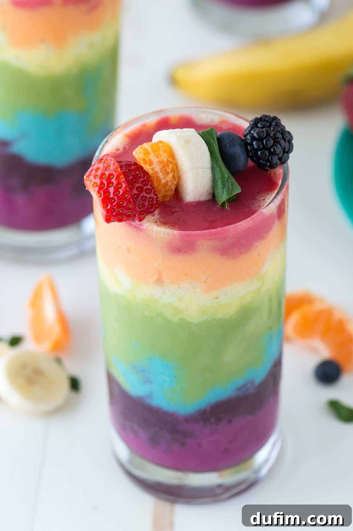 Beautiful 7 layer rainbow smoothie recipe! Full of tons of fruit and topped with a fruit skewer, it’s the ultimate rainbow smoothie! A stunning seven-layer rainbow smoothie, elegantly presented in a tall glass, crowned with a vibrant skewer of strawberry, orange, banana, spinach, blueberry, and blackberry.