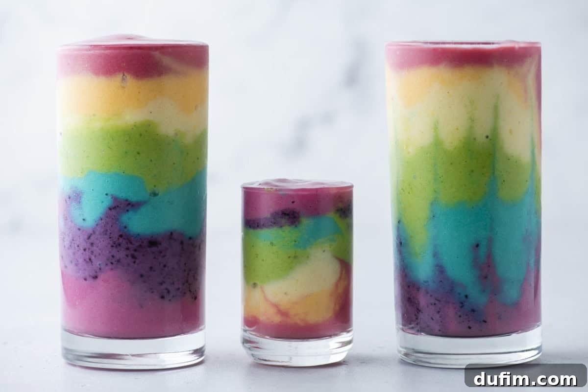 Colorburst Smoothie Delight 3 Three rainbow smoothies in elegant glass cups, arranged on a clean white background, creating a stunning visual display of vibrant colors.