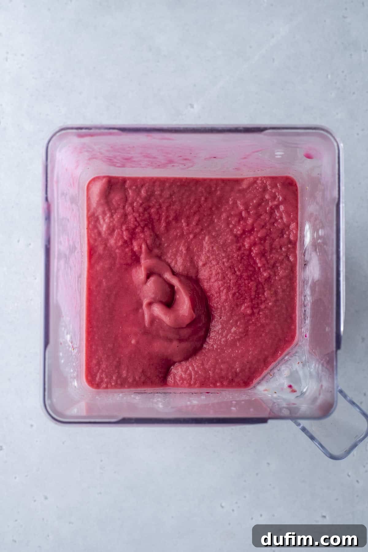 The first layer, a rich red smoothie, is gently poured into the bottom of a tall glass, forming a solid base for the rainbow.