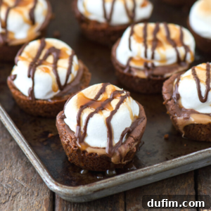 Miniature turtle smores bites dessert cups topped with toasted marshmallows and drizzled with chocolate and caramel sauce, arranged on a rustic metal baking sheet.