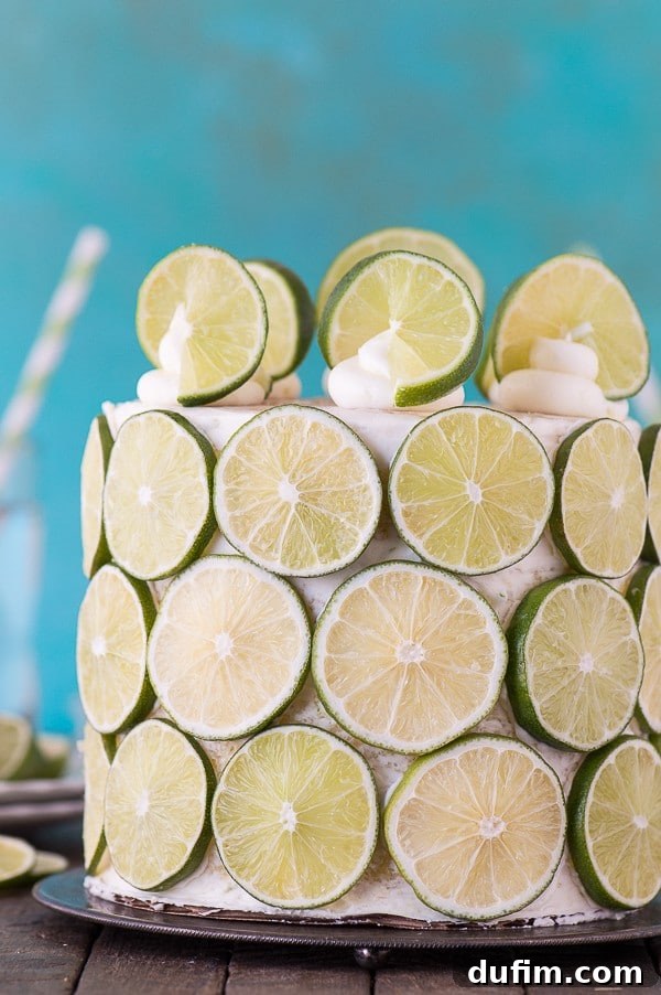 Side view of the partially frosted coconut lime cake, highlighting the delicate layers and the vibrant green of the fresh lime slices beginning to be applied.