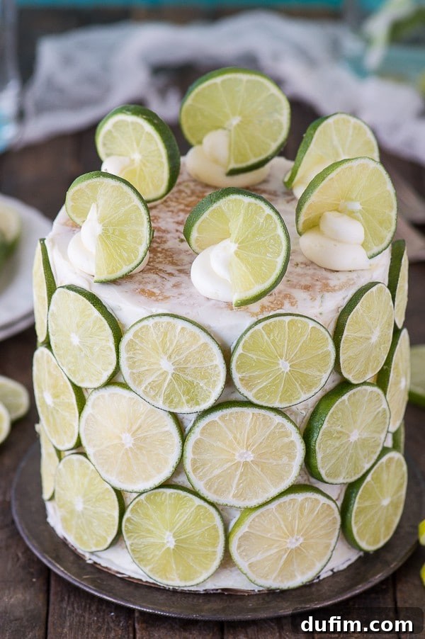 A closer view of the finished coconut lime cake, displaying its textured lime buttercream and artfully placed lime slices, with swirls of frosting on top.
