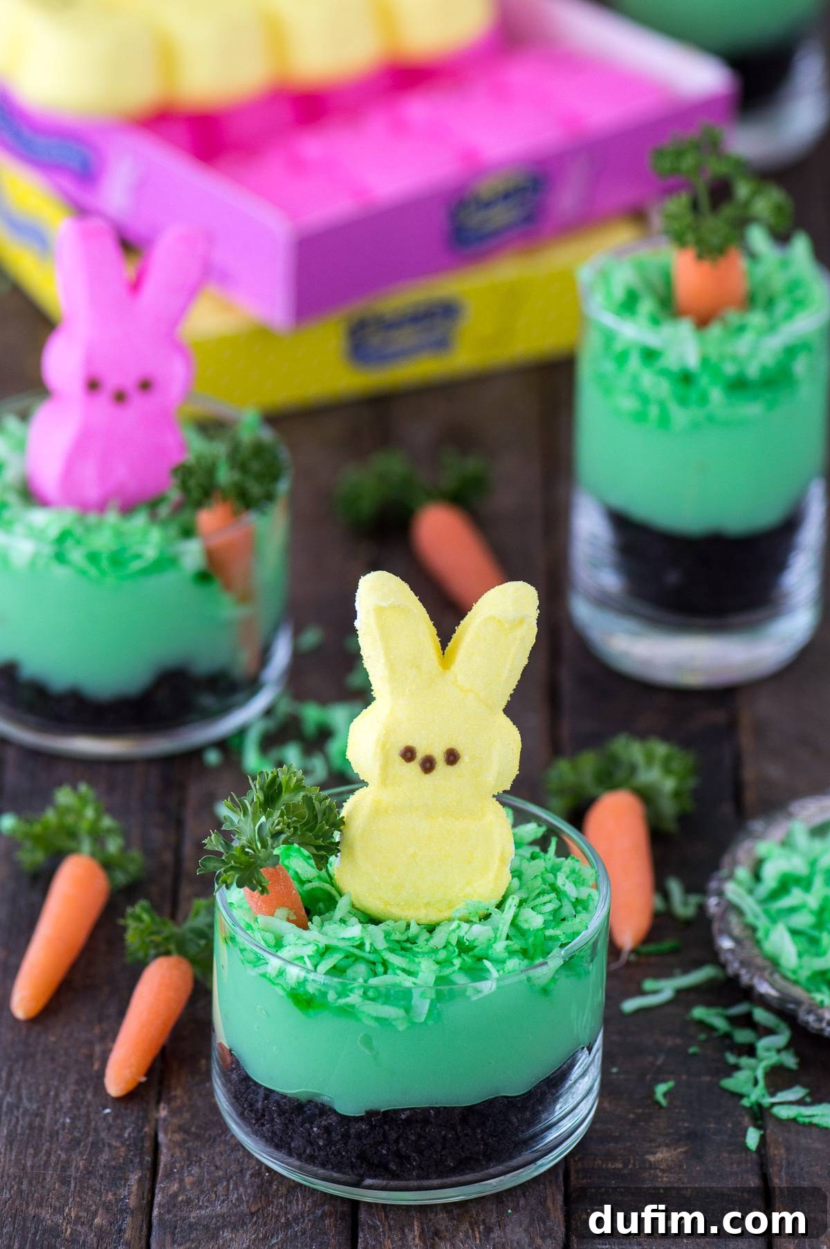 Close-up of a festive Peeps Bunny Pudding Cup, featuring crushed Oreos, vibrant green pudding, shredded coconut, a miniature carrot with parsley greens, and an adorable pink Peeps bunny, all served in a clear glass bowl for a perfect no-bake Easter dessert.