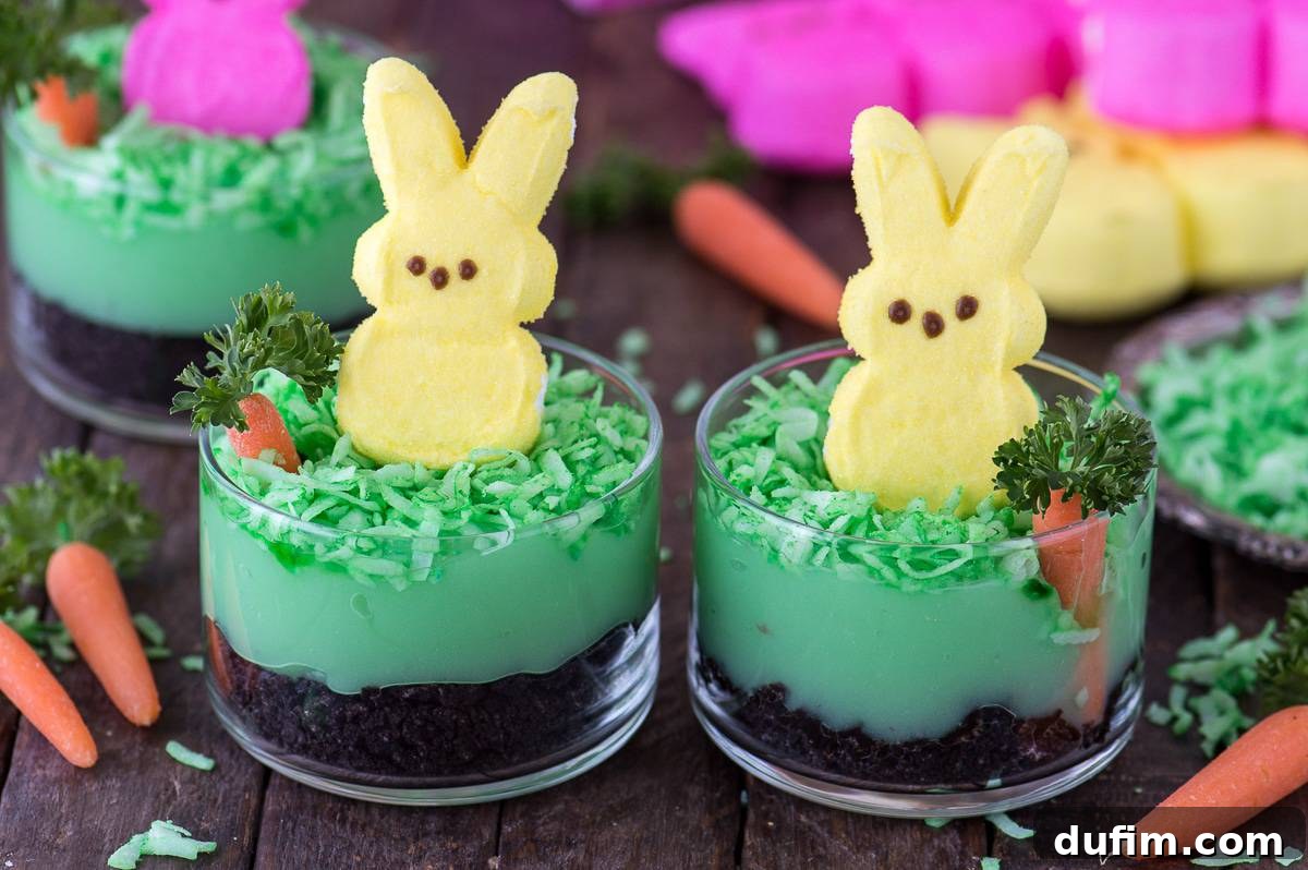 Overhead shot of two beautifully crafted Peeps Bunny Pudding Cups, showcasing the layered ingredients including 'dirt' (crushed Oreos), green 'grass' (dyed coconut), creamy pistachio pudding, edible carrots, and bright Peeps bunnies, ready for Easter celebrations.