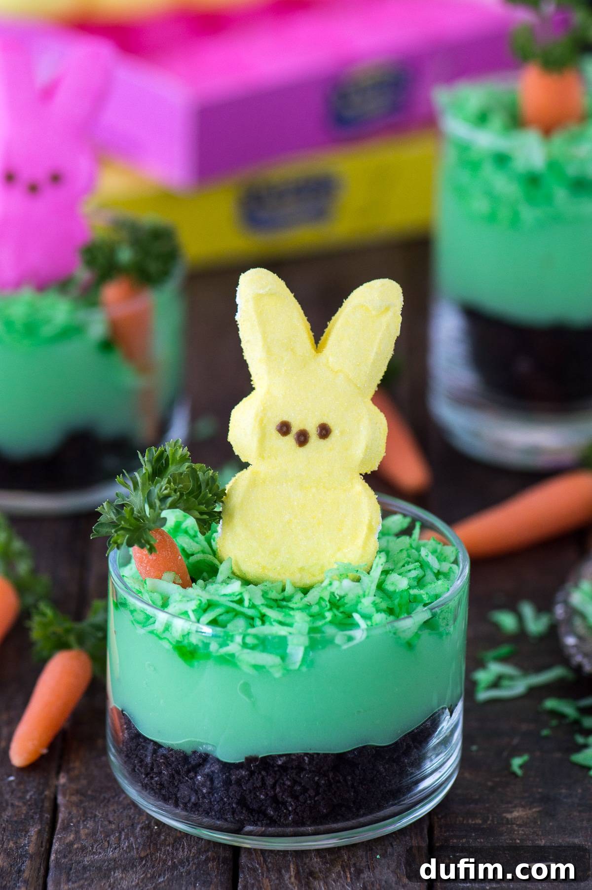 A single Peeps Bunny Pudding Cup presented in a clear glass, highlighting the colorful layers of cookie crumbs, green pudding, and coconut, crowned with a playful pink Peeps bunny, ideal for a sweet spring celebration.