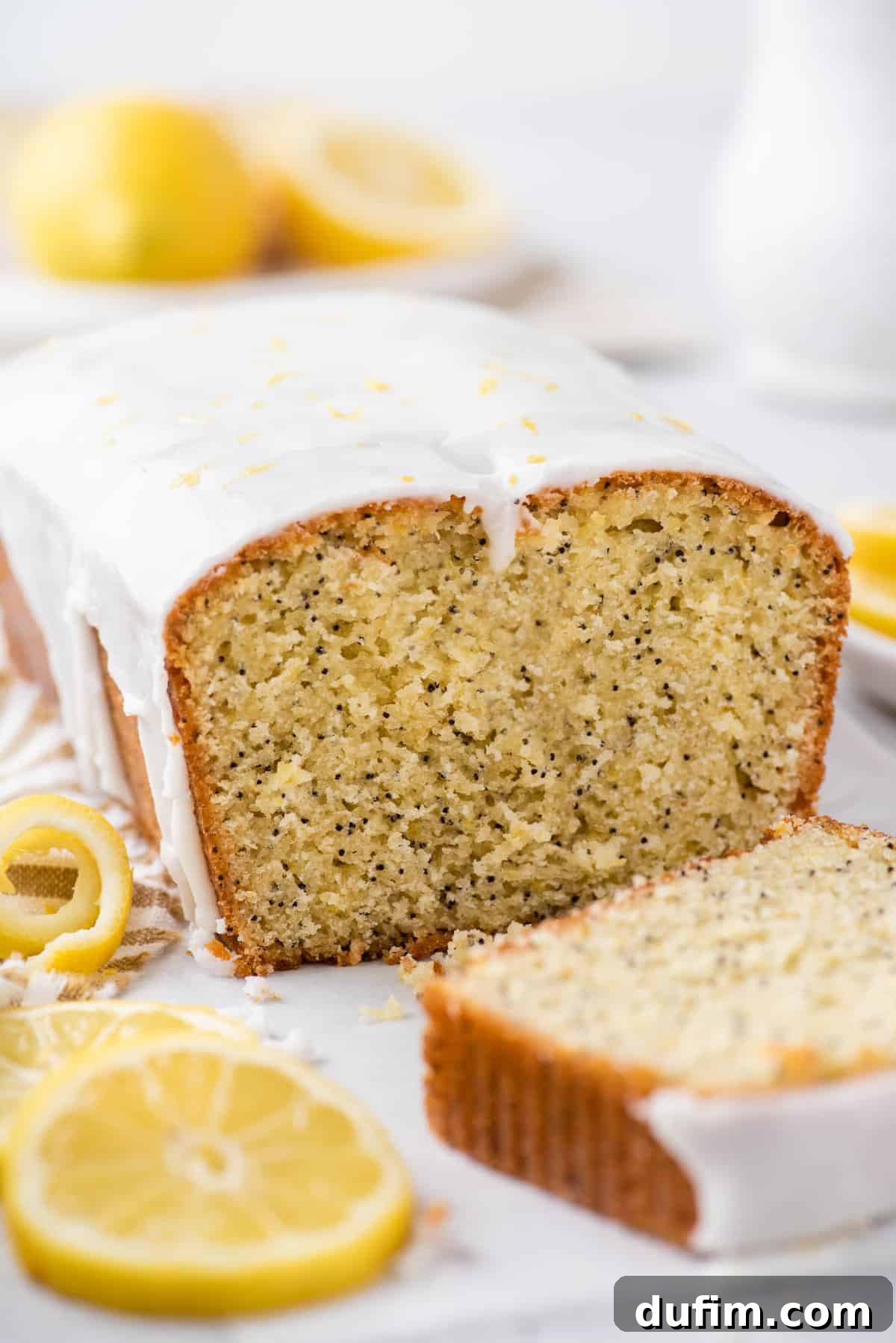 A loaf of freshly baked Lemon Poppy Seed Bread with a slice cut, revealing its moist and tender interior.