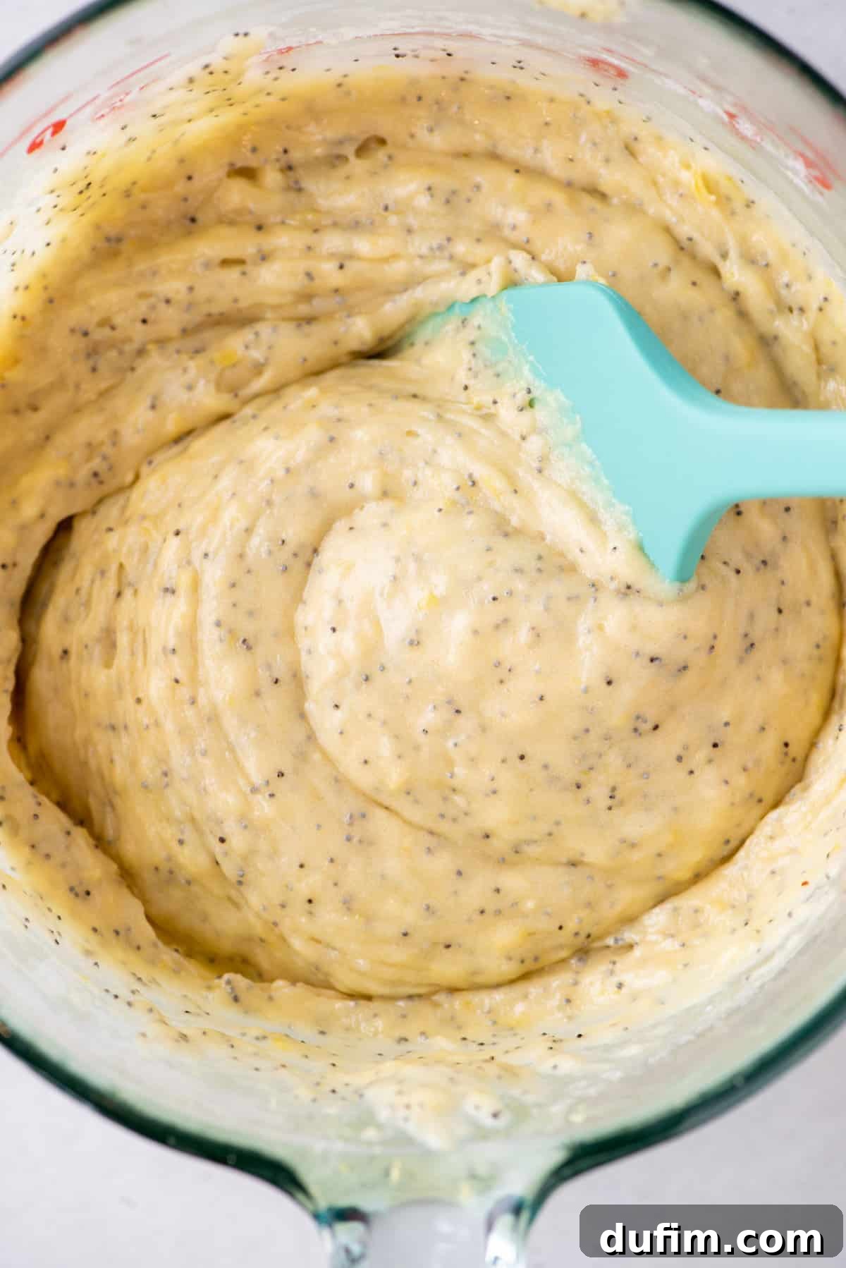 Lemon poppy seed batter in a glass mixing bowl with a rubber spatula, ready for baking.