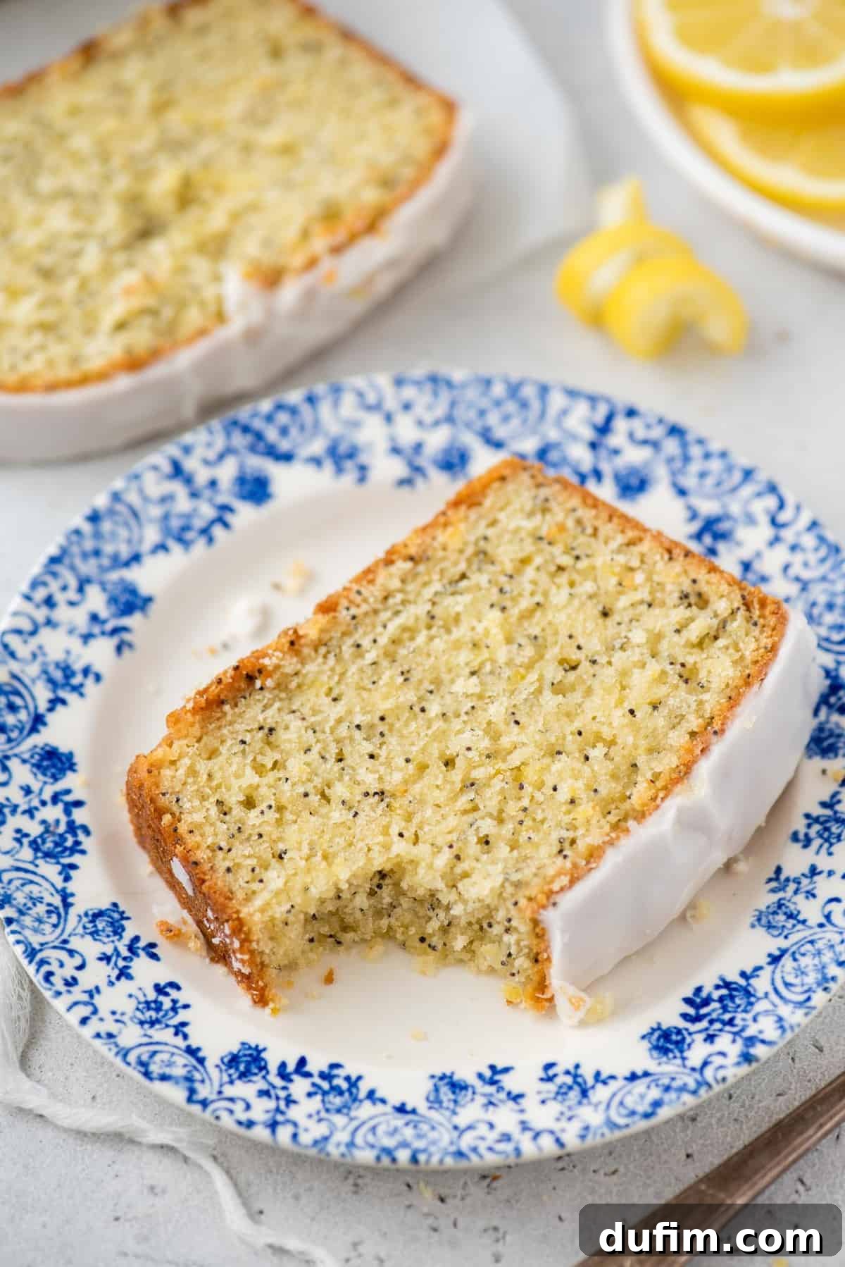 A slice of glazed lemon poppy seed bread on a plate with a bite taken out, emphasizing its deliciousness.