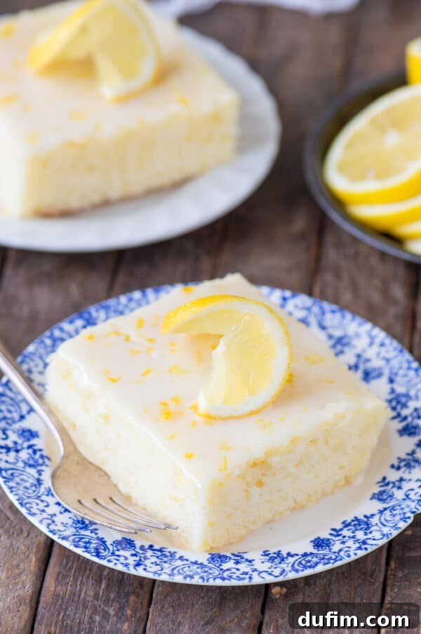 A delightful piece of lemon cake generously coated with a glistening lemon glaze, elegantly presented on a blue floral plate against a rustic wood background.