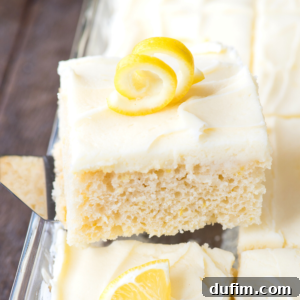 A square piece of lemon cake with creamy white frosting and a decorative lemon twist on top, being lifted from a tray of delicious lemon cake pieces.