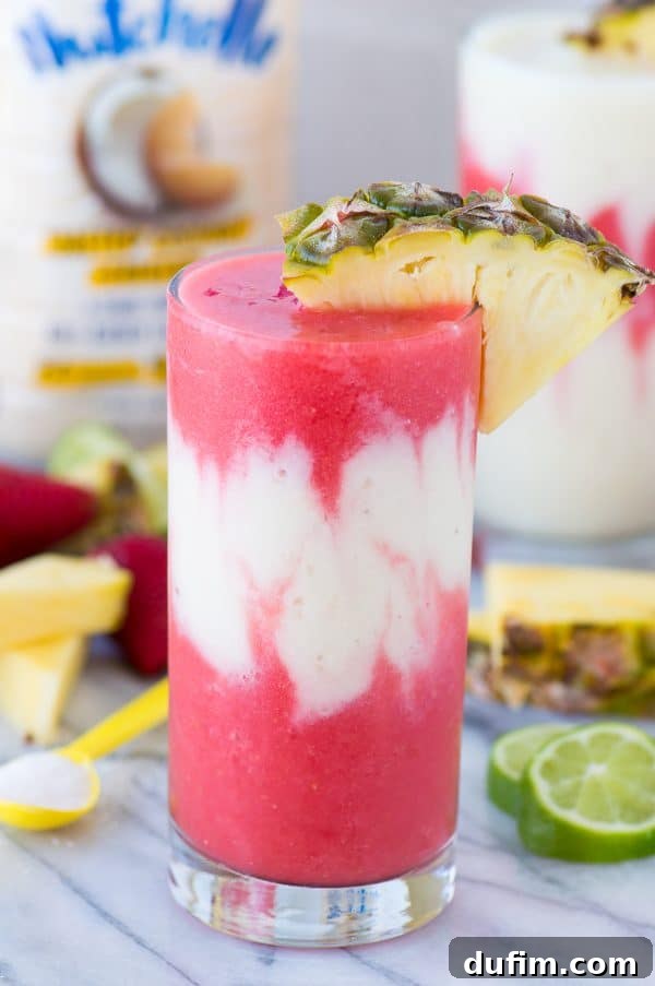 A hand pouring the creamy pina colada layer into a glass, carefully separating it from the strawberry daiquiri layer to create the iconic Miami Vice Mocktail.